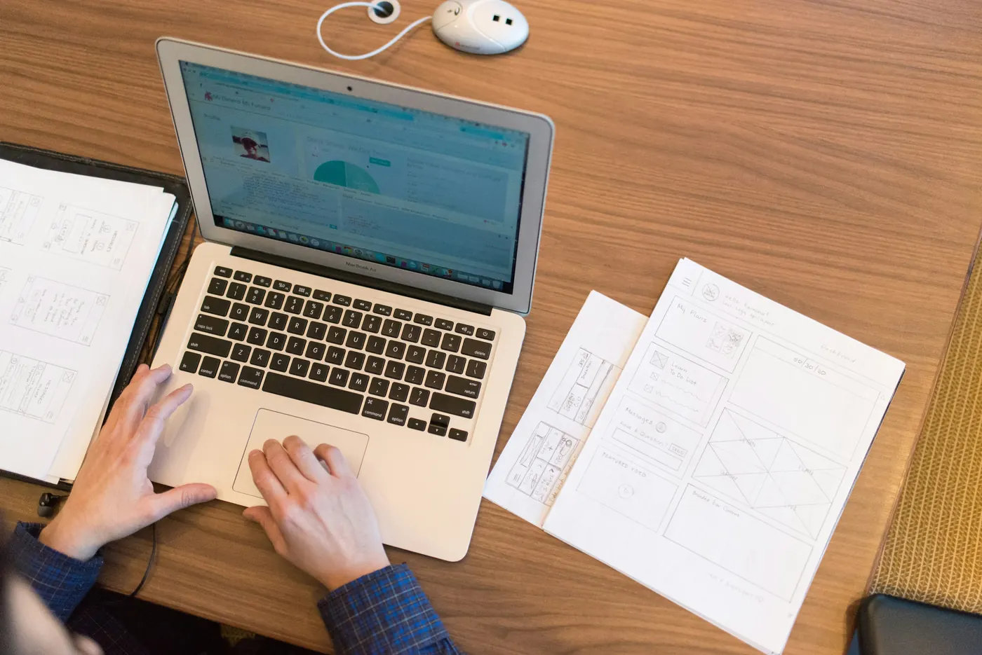 Person working on a laptop beside hand-drawn website wireframes