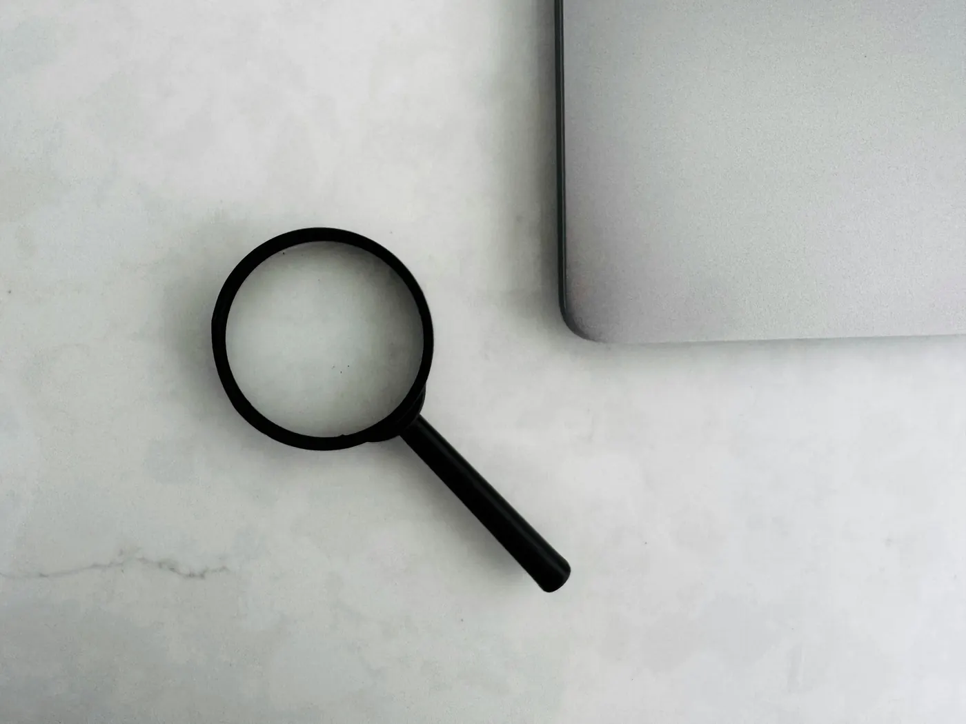 Magnifying glass beside a laptop on a workspace